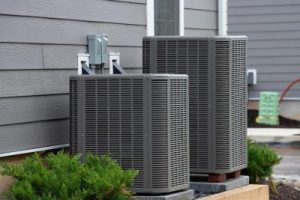 Two air conditioners sit outside a gray house